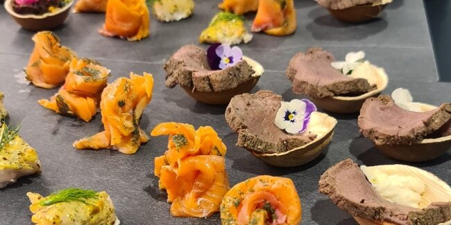 Et langbord dekket med et stort utvalg av appetittvekkere, inkludert laks, kjøtt og grønnsaker, vakkert presentert med spiselige blomster.