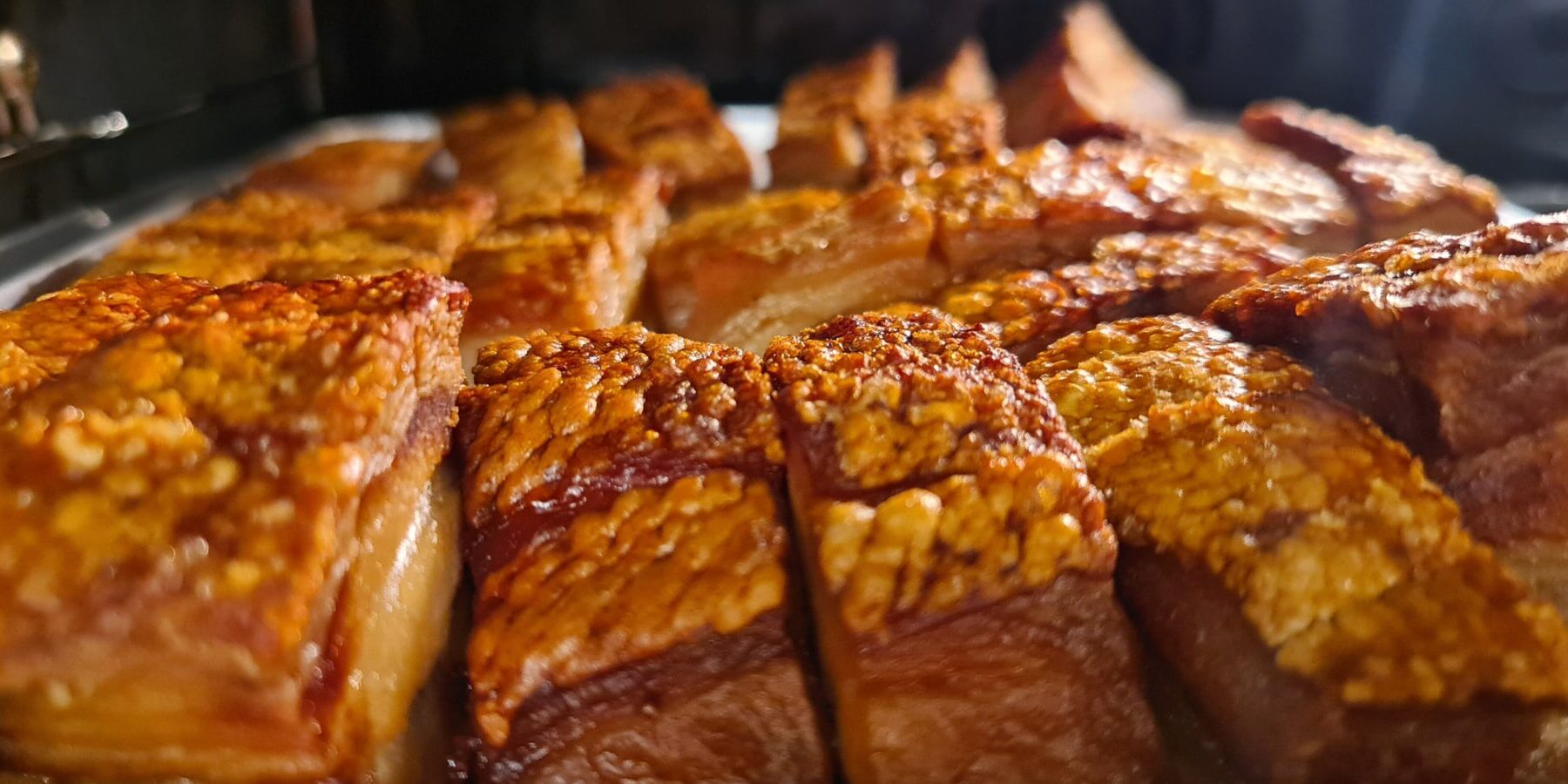 Nærbilde av sprøstekt ribbe i ovnen, med gyllen og knasende svor, klar for servering